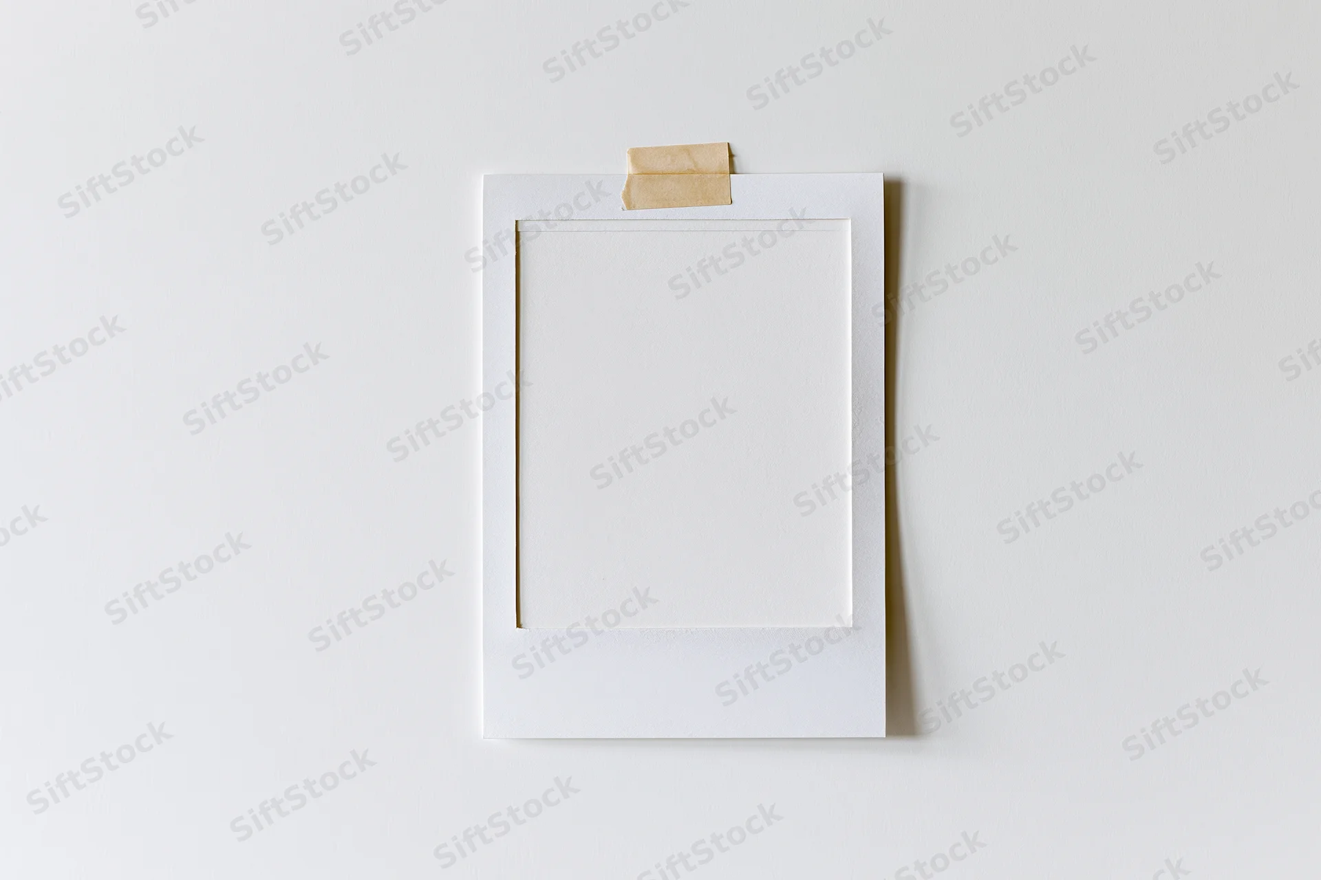 Blank white polaroid photo print taped to a white wall