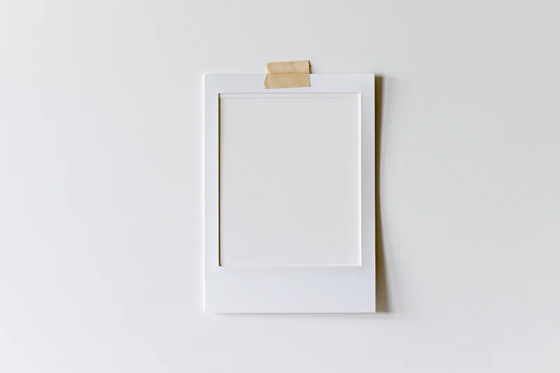 Blank white polaroid photo print taped to a white wall