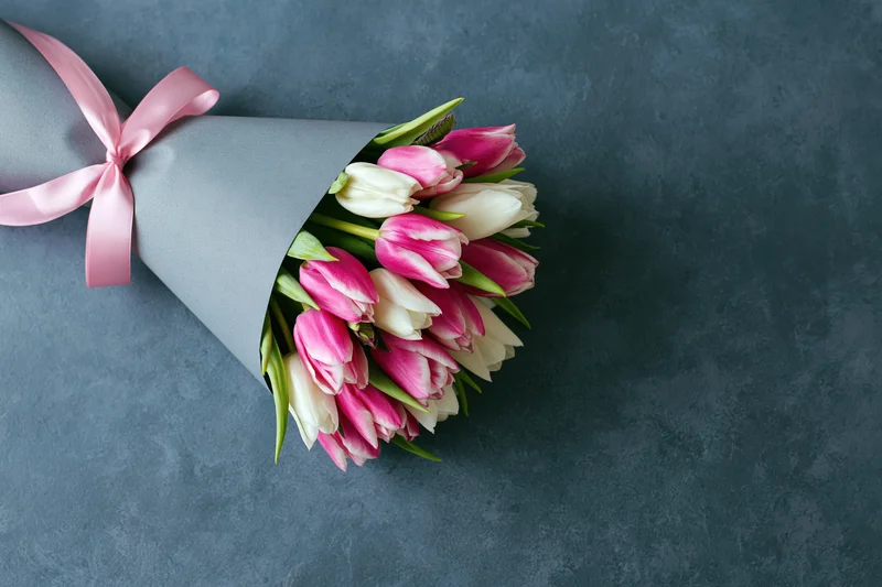 Bouquet of pink and white tulips wrapped in grey matte paper on textured surface