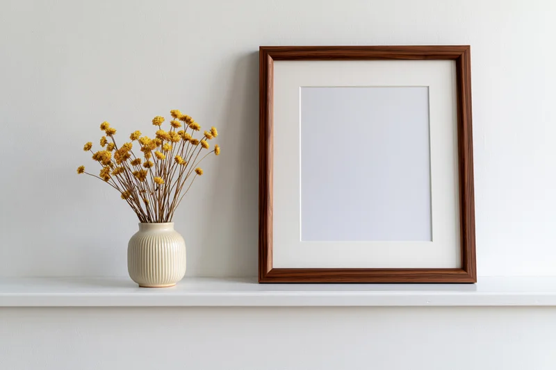 Dark walnut wood frame with white mat and dried yellow flowers in ceramic vase on white shelf