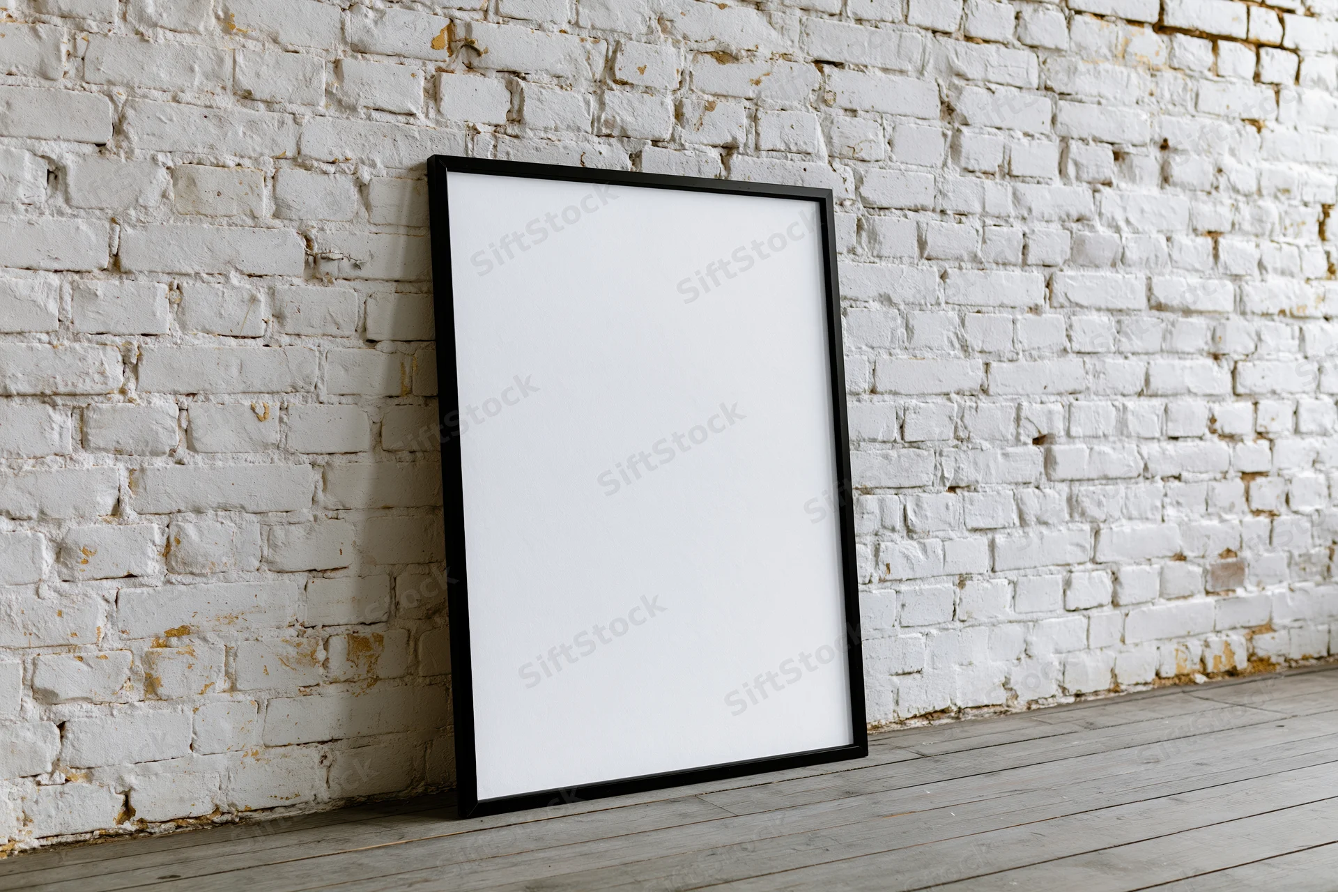 Black-framed blank poster leaning against white brick wall in studio space