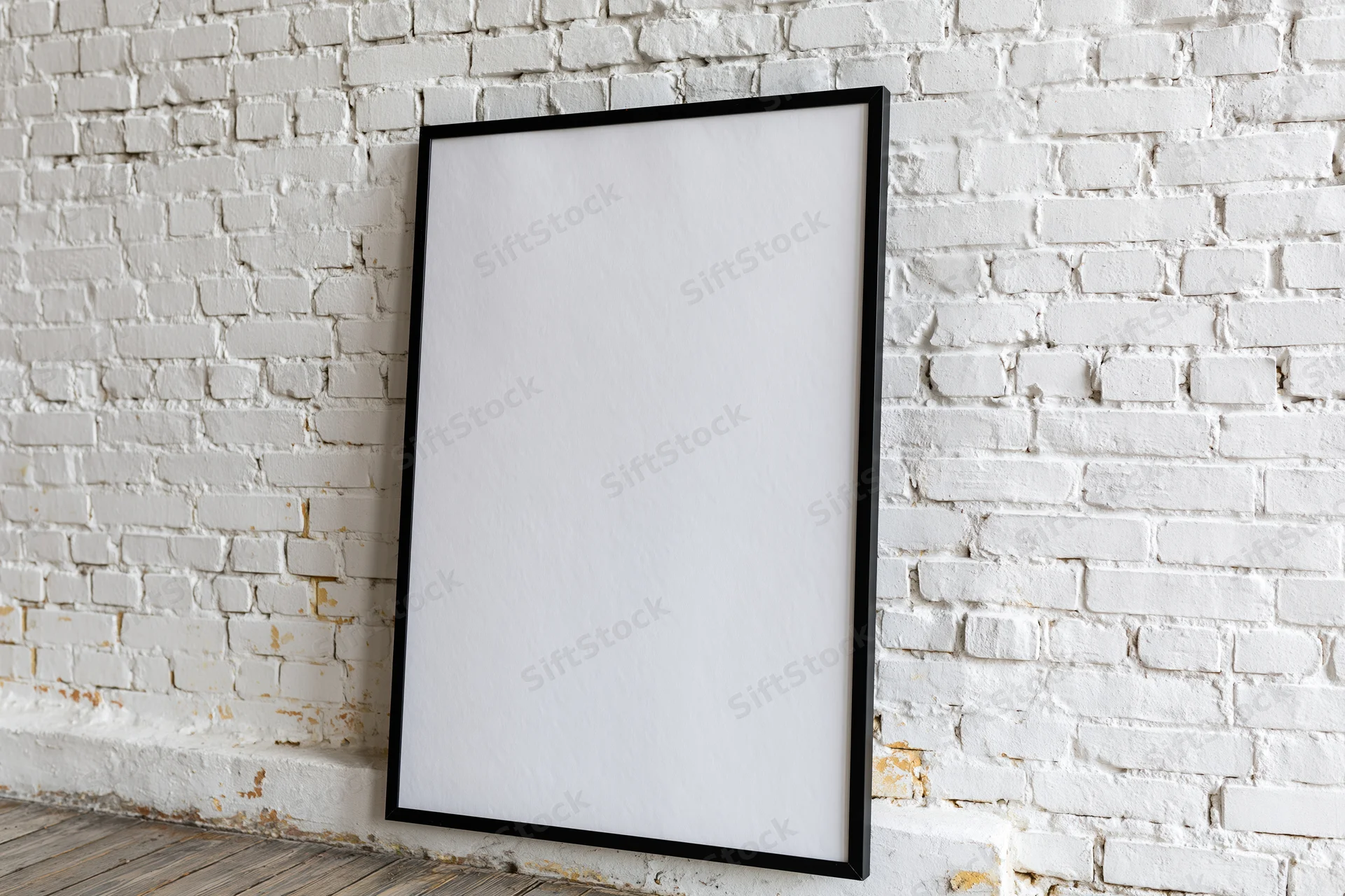 Black-framed blank poster leaning against white brick wall in interior space