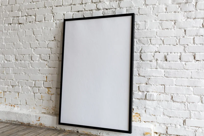 Black-framed blank poster leaning against white brick wall in interior space