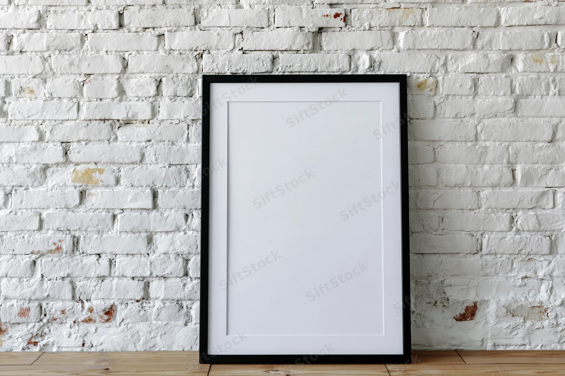 Black-framed blank poster leaning against white brick wall on wooden floor
