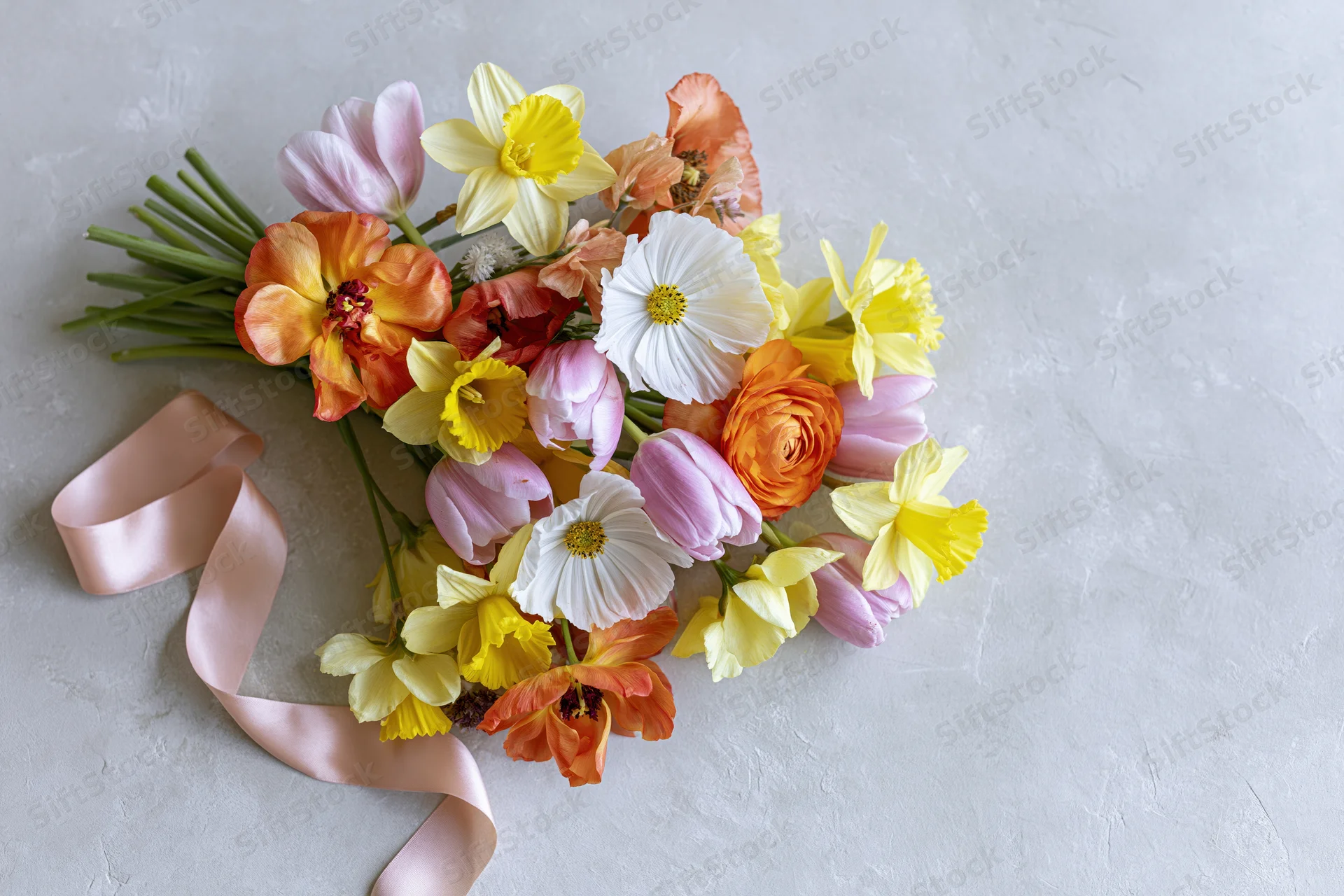 Loose bouquet of mixed spring flowers with pastel ribbon on light textured surface