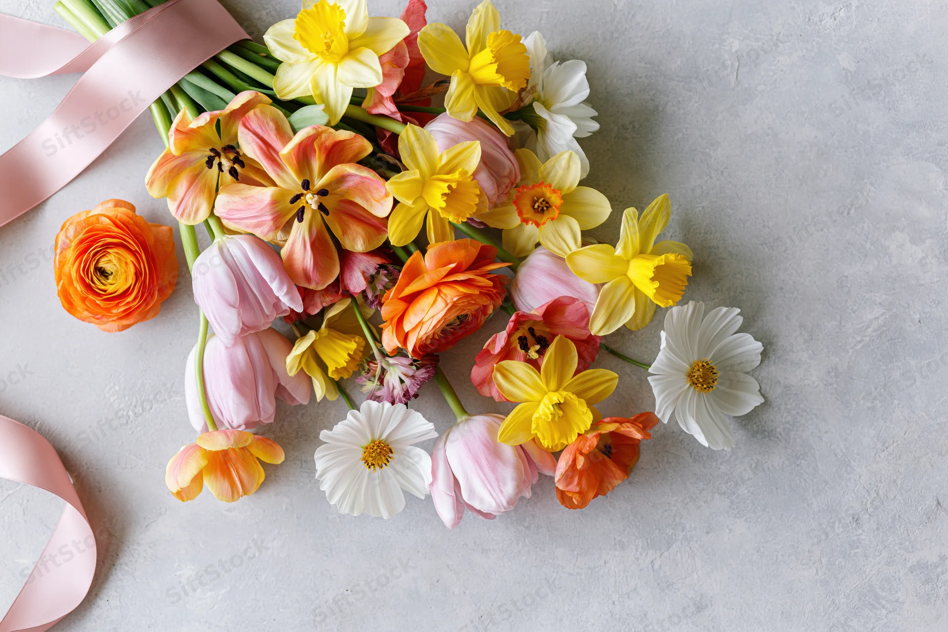 Loose bouquet of mixed spring flowers with pink ribbon on concrete surface