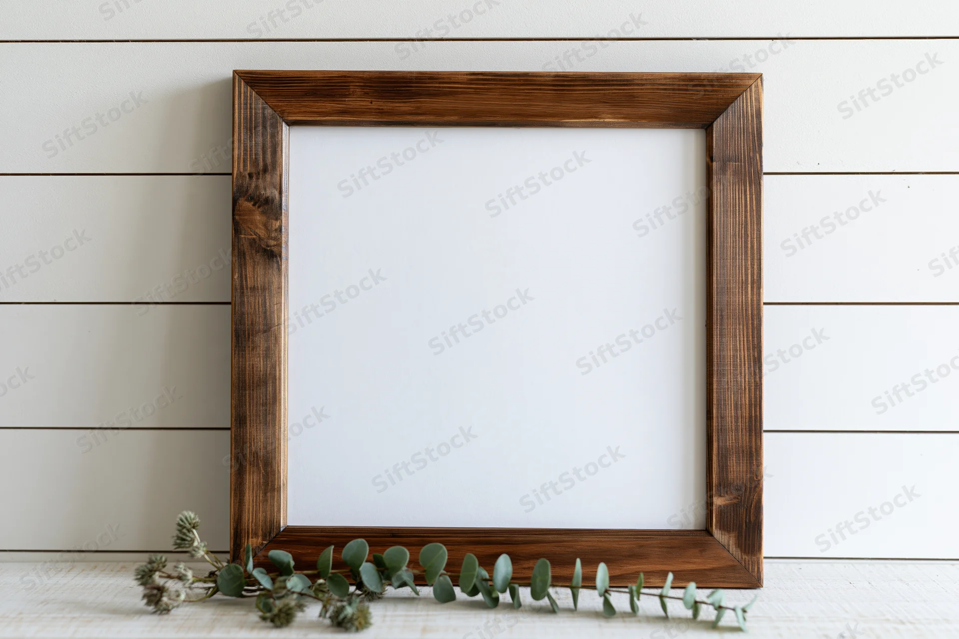 Dark stained wooden frame with blank white interior and eucalyptus branch on shiplap wall
