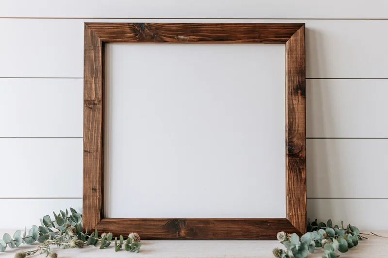 Rustic dark-stained wooden frame with blank white interior on shiplap wall, flanked by eucalyptus branches