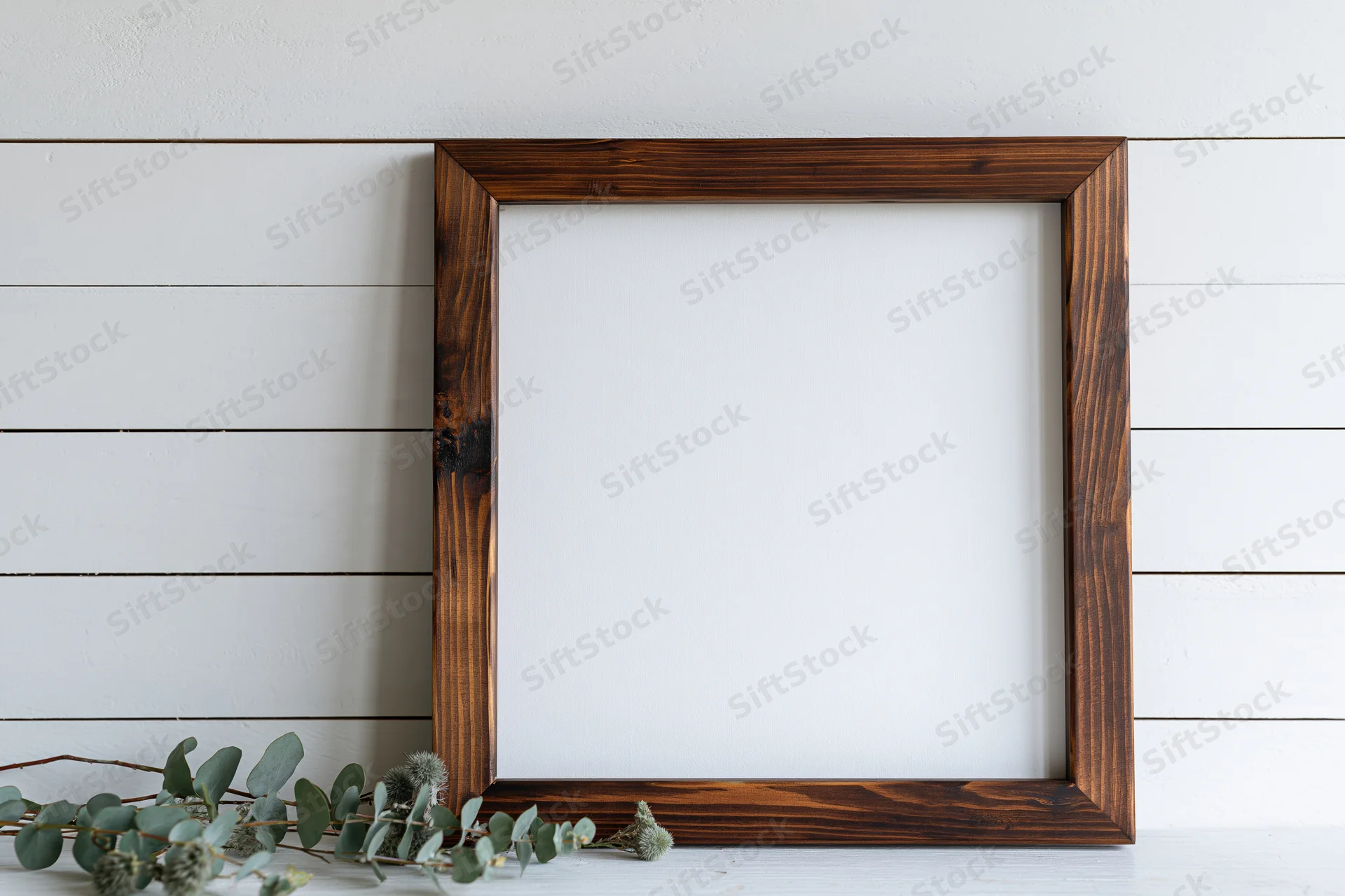 Dark stained wooden frame with blank white interior on white shiplap wall, eucalyptus branch beside it