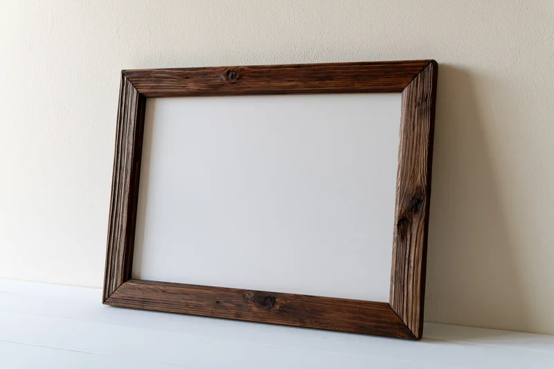 Dark rustic wood picture frame with blank white interior leaning on a shelf against a wall