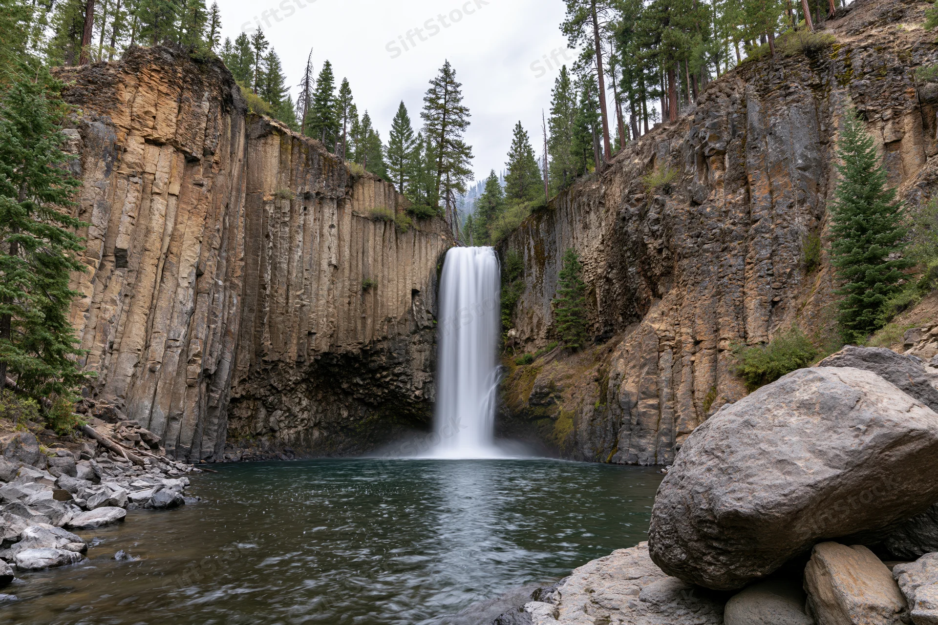 Waterfall dropping into calm pool at base of rocky canyon surrounded by pine forest