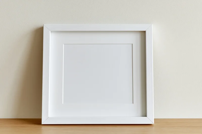 White square picture frame with white mat leaning against a beige wall on wooden surface