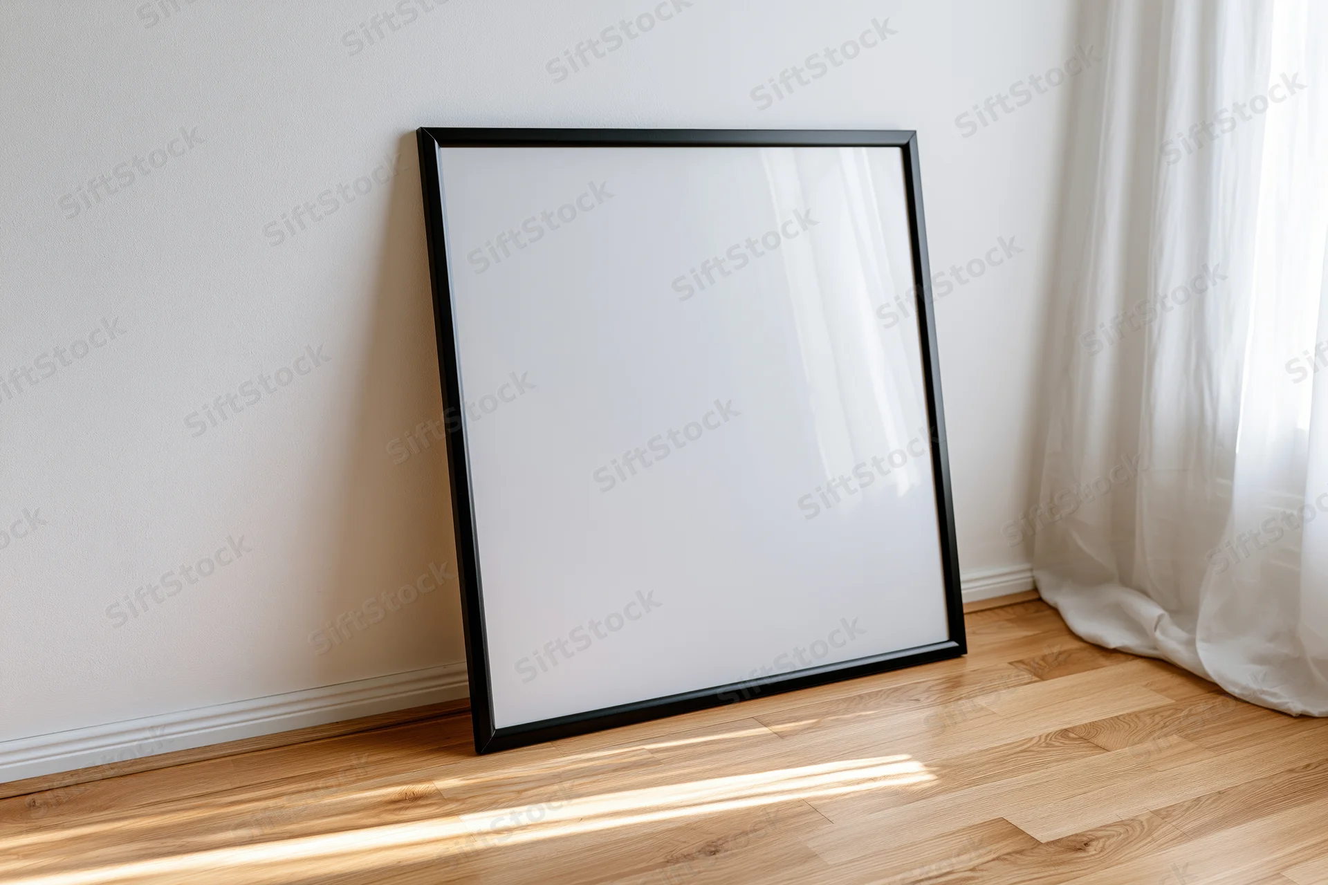 Black frame with blank white surface leaning against wall in sunlit room with wooden floor and sheer curtain