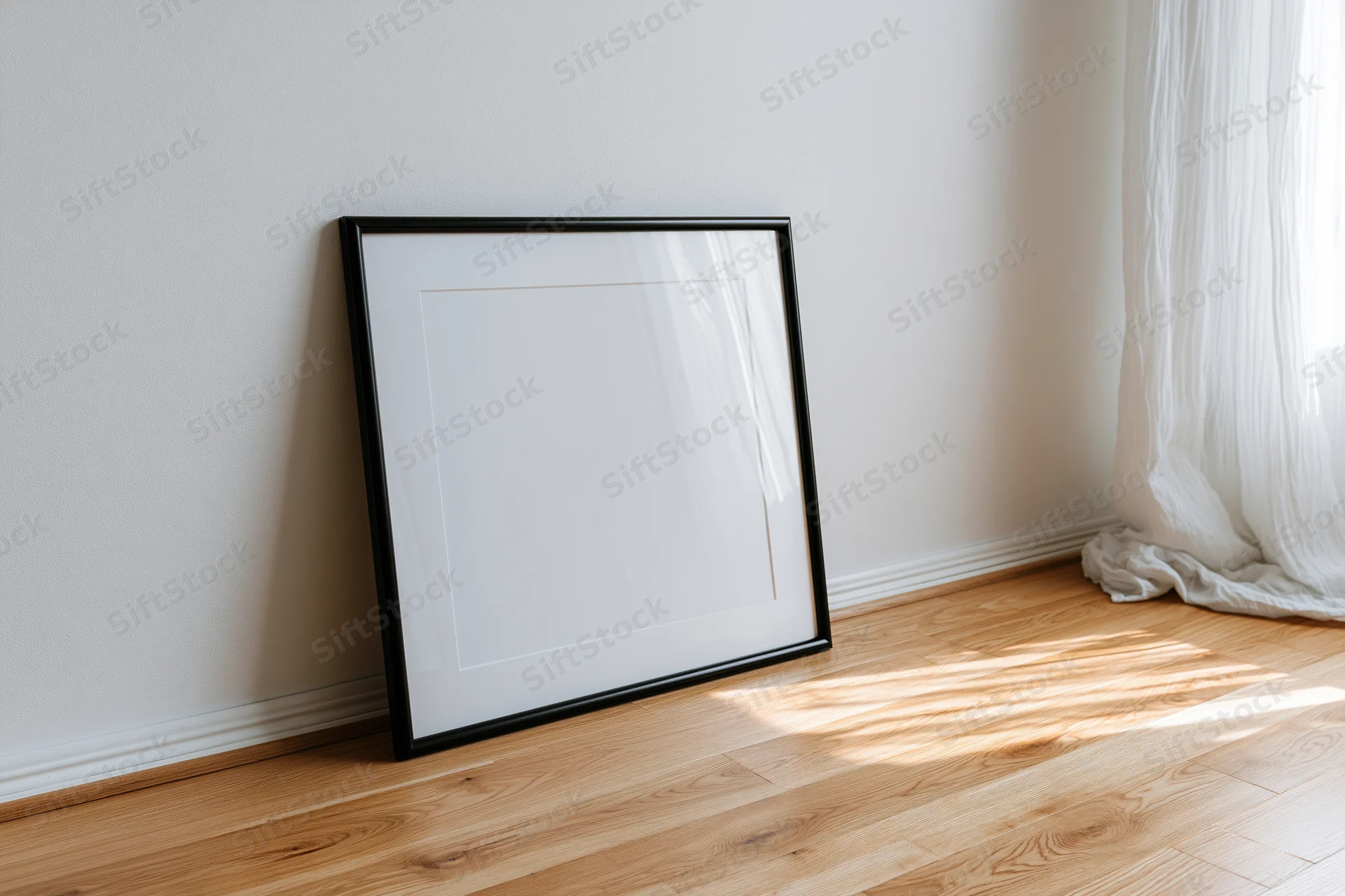 Black picture frame leaning against white wall on wooden floor near window with sheer curtain