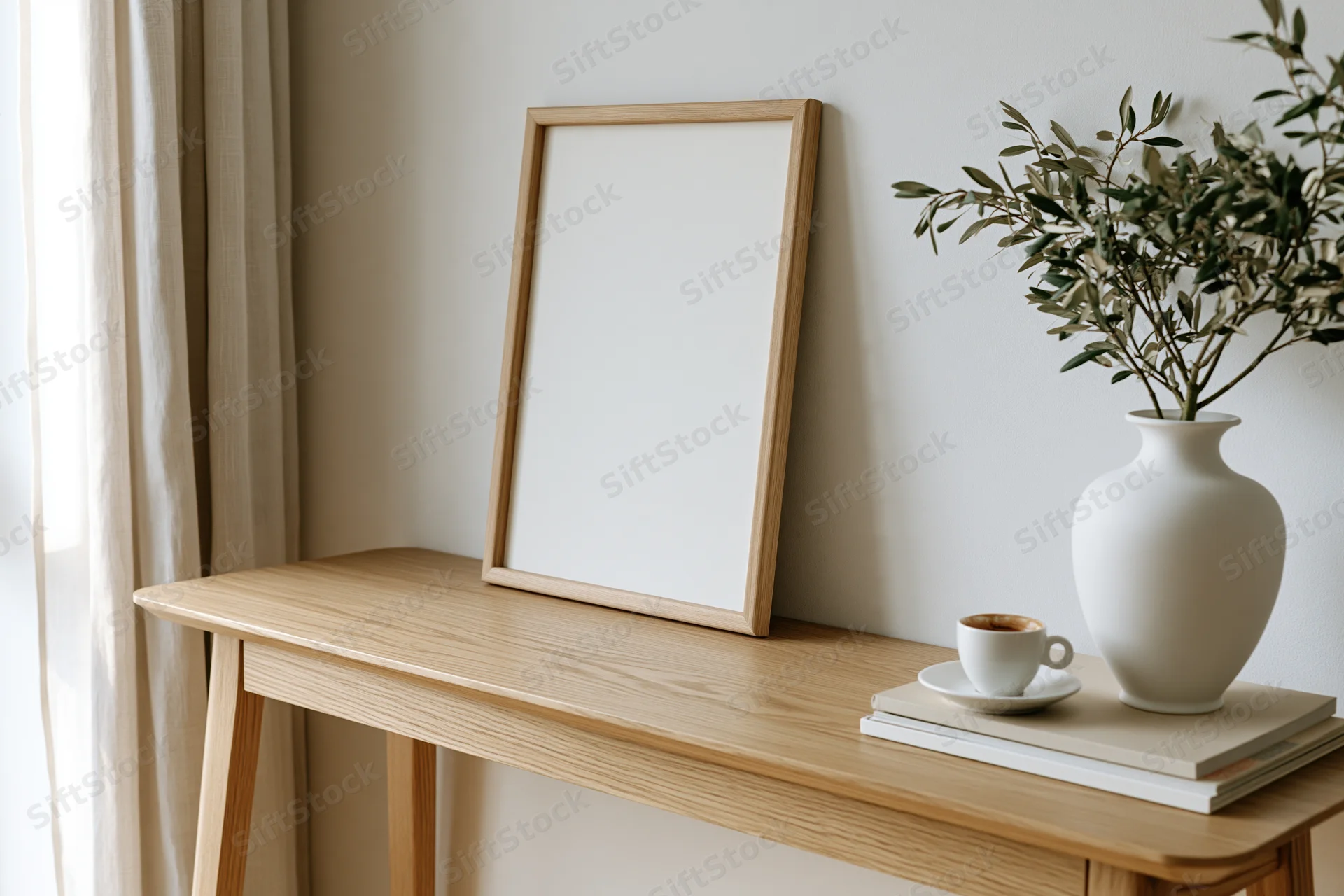Wooden frame leaning against white wall on a desk with vase of olive branches, coffee cup, and books