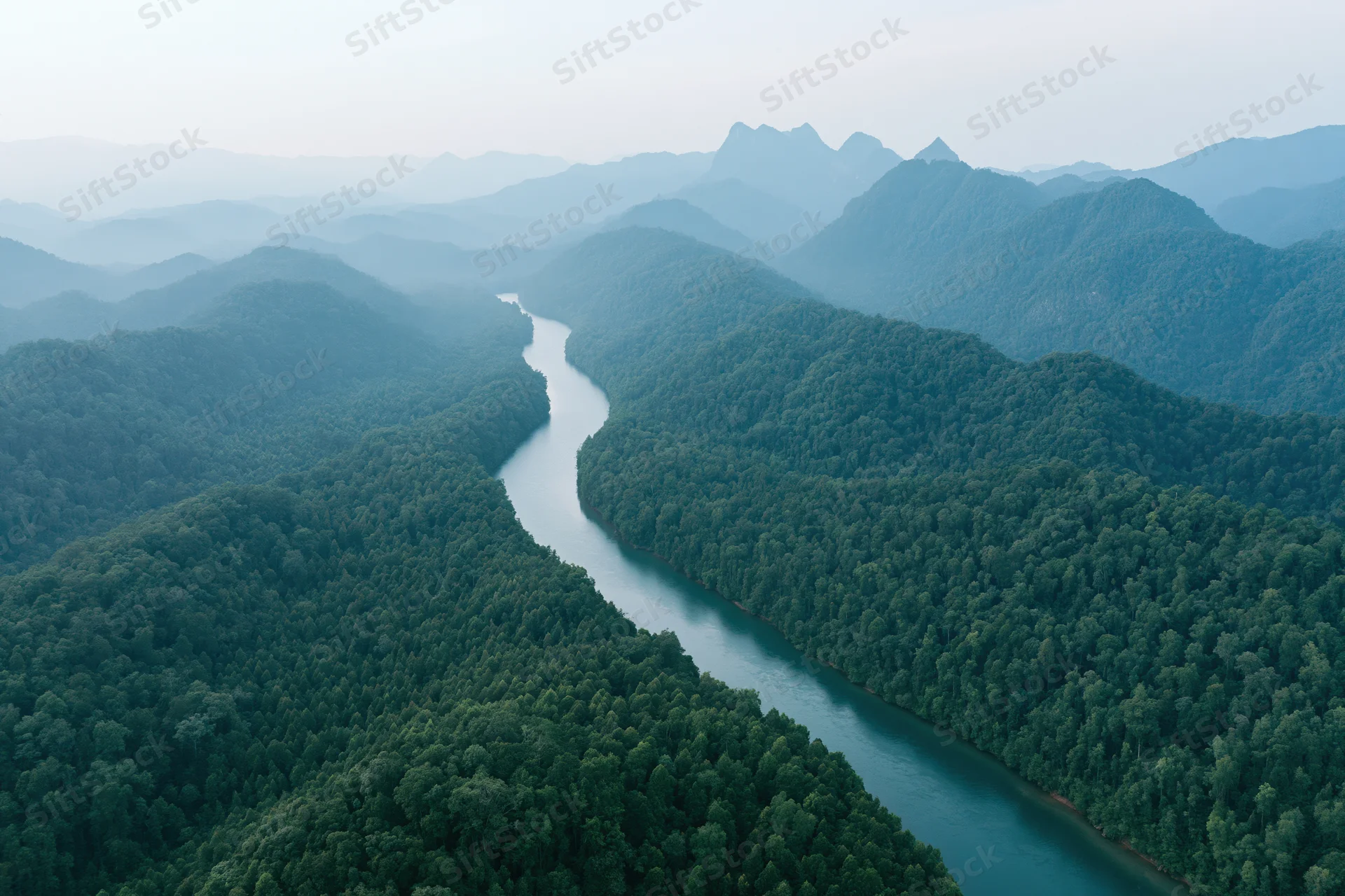 Winding river cutting through dense tropical forest with mountains in the distance