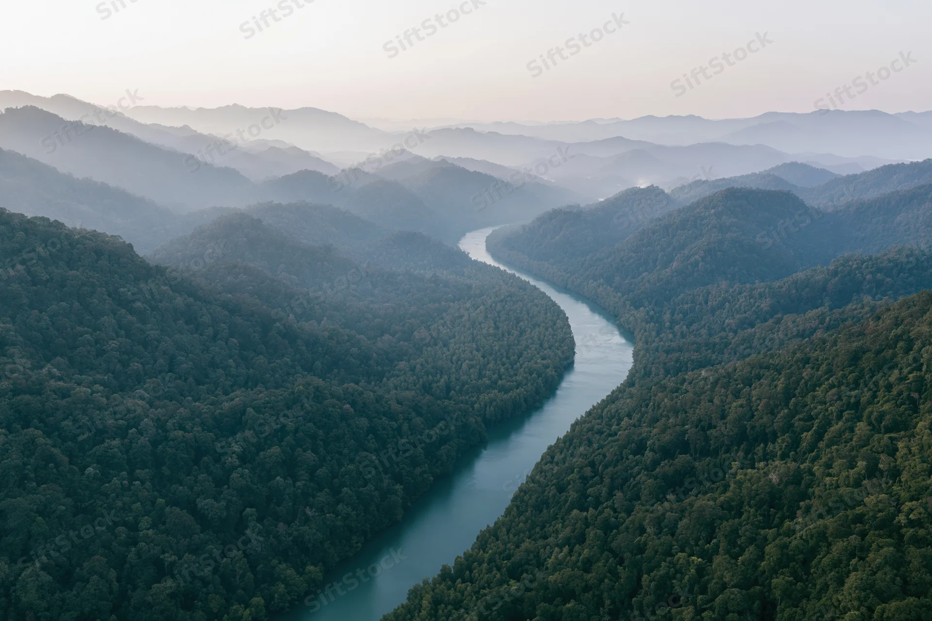 Aerial view of a winding river cutting through dense tropical forest surrounded by mountains