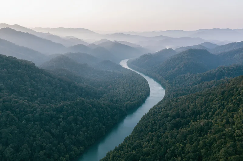 Aerial view of a winding river cutting through dense tropical forest surrounded by mountains