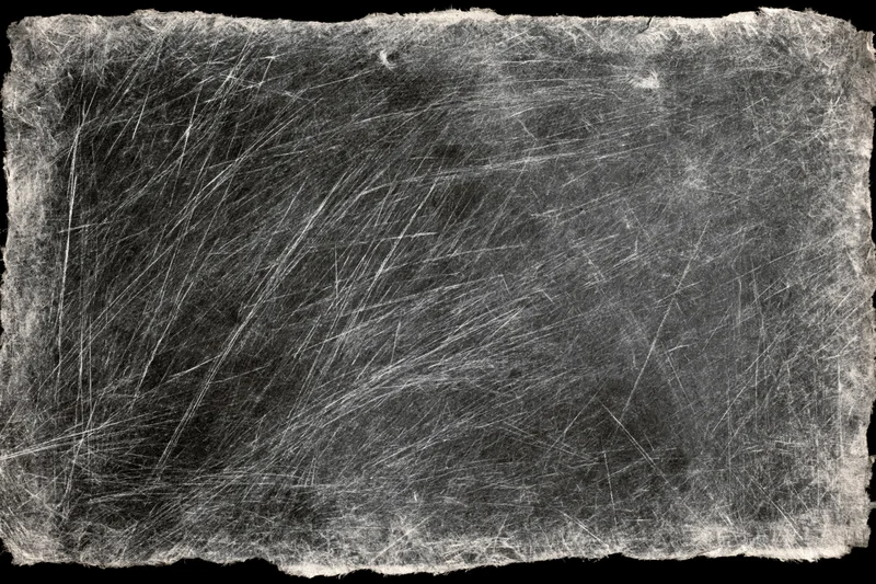 Heavily scratched and worn darkroom photographic paper with fibrous edges and monochrome texture