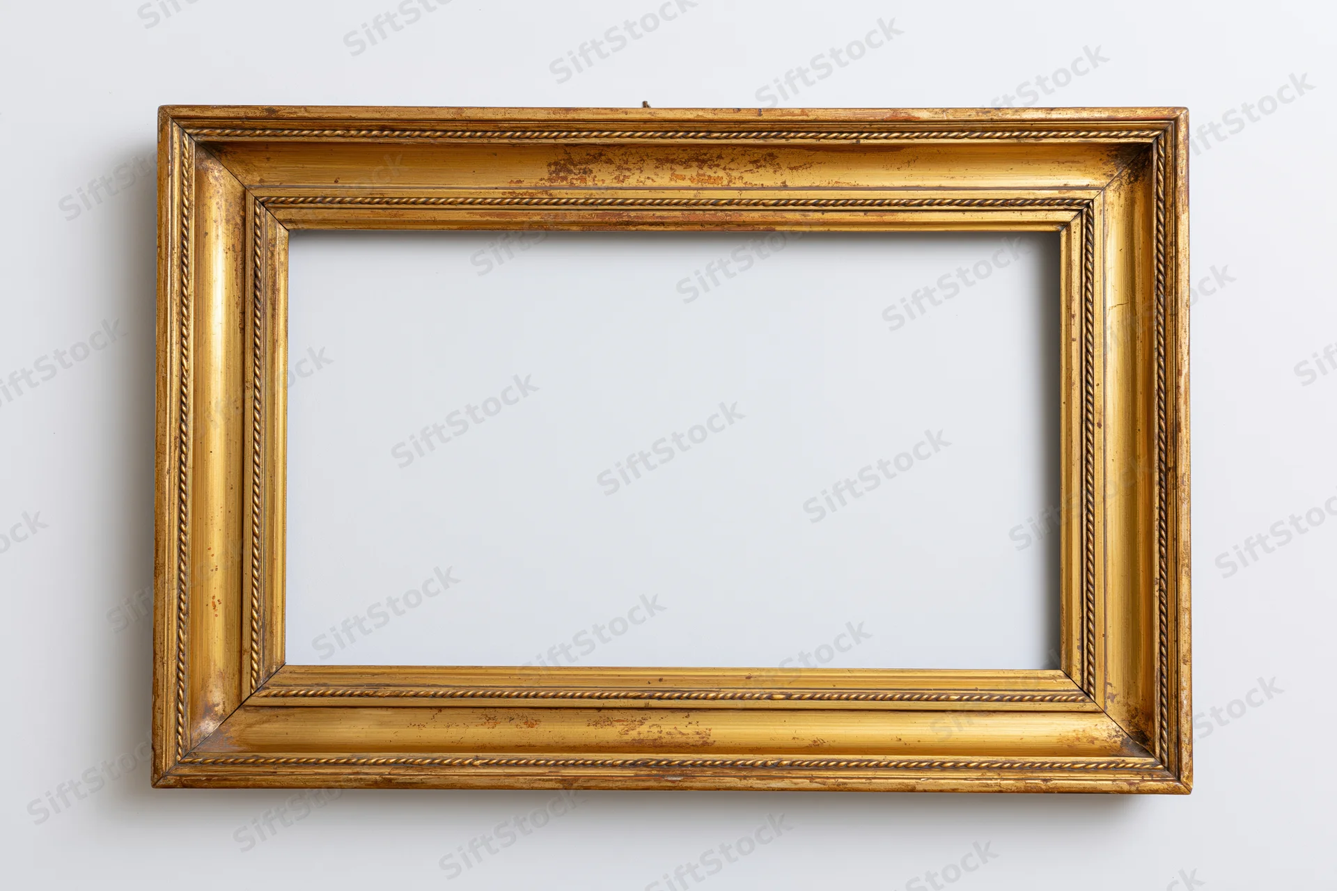 Ornate antique gold picture frame with empty interior hanging on white wall