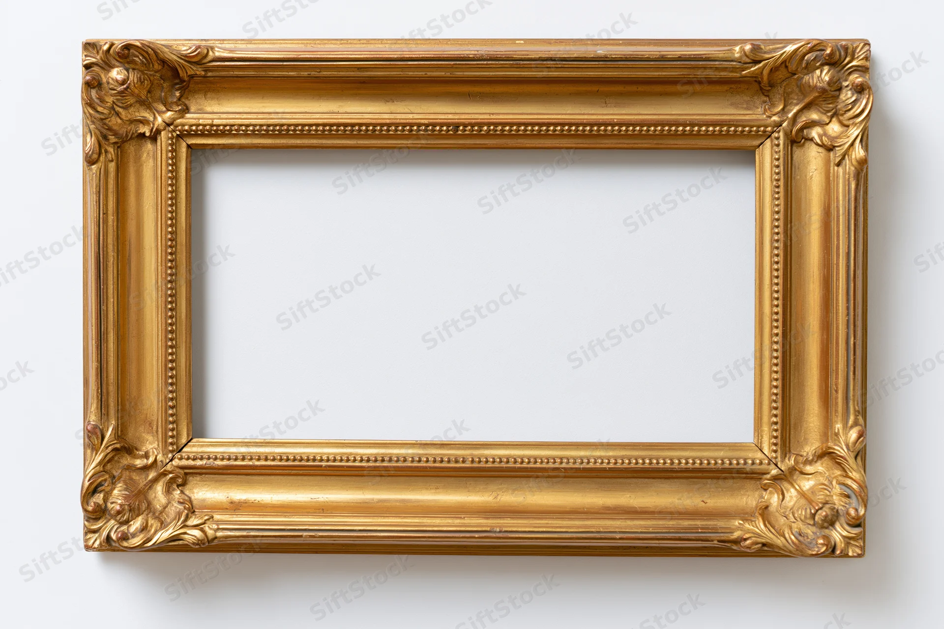Ornate gold picture frame with carved floral corners hanging on white wall