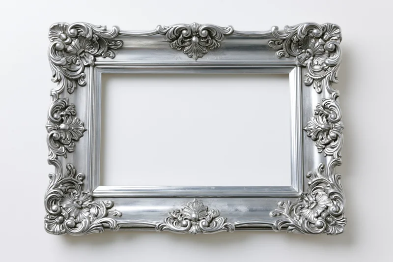 Ornate silver baroque frame with intricate scrollwork hanging on white wall