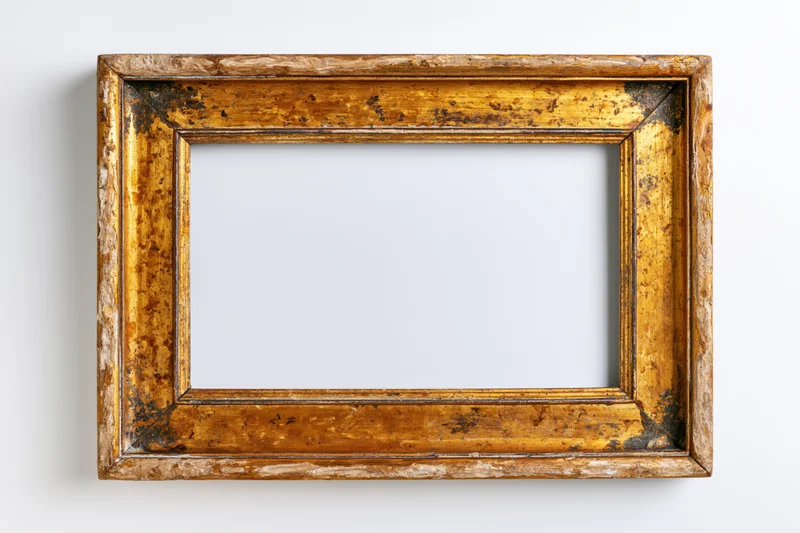 Antique wooden picture frame with worn gold-bronze finish hanging on white wall
