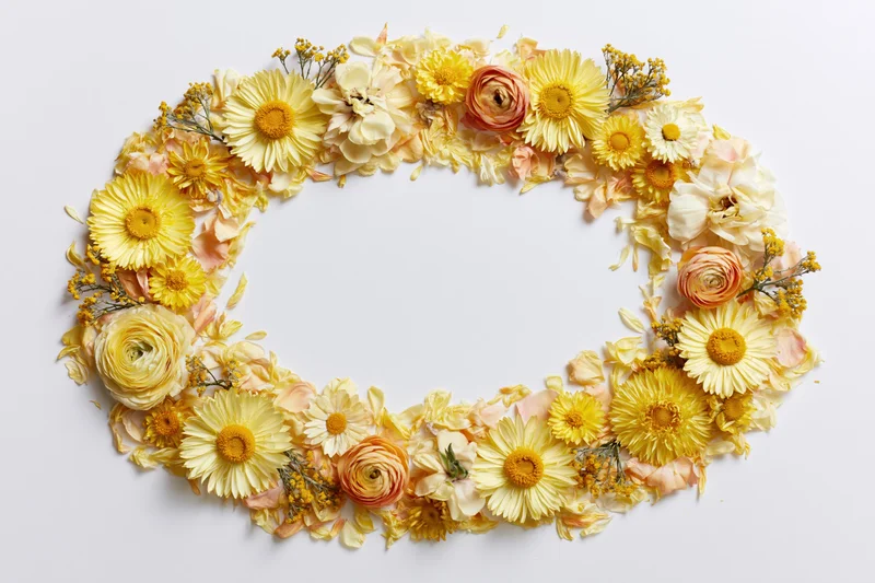 Loose oval floral arrangement of yellow and peach flowers on white background with central copyspace