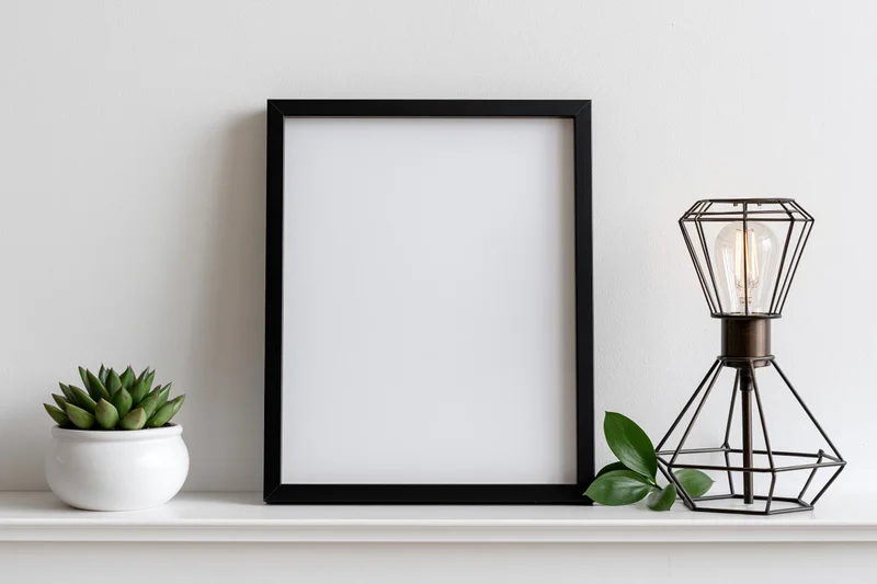 Black frame with blank white interior on white shelf beside succulent and wire lamp