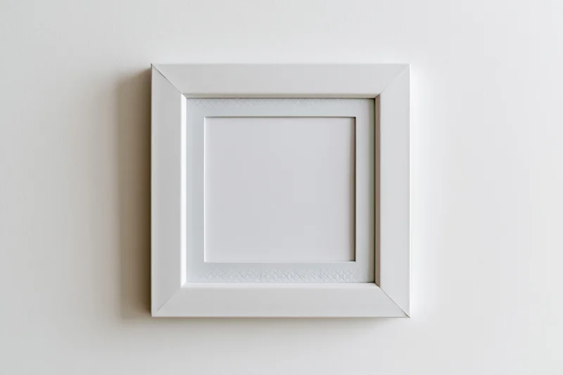 White square photo frame hanging on a plain wall with blank interior and visible shadow