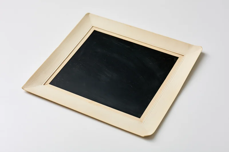Square chalkboard with wooden frame lying flat on white surface