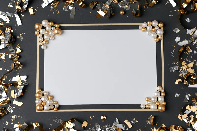 Blank white card framed with gold and silver pearls and confetti on dark surface