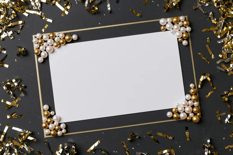 Blank white card framed with pearls and gold confetti on dark surface