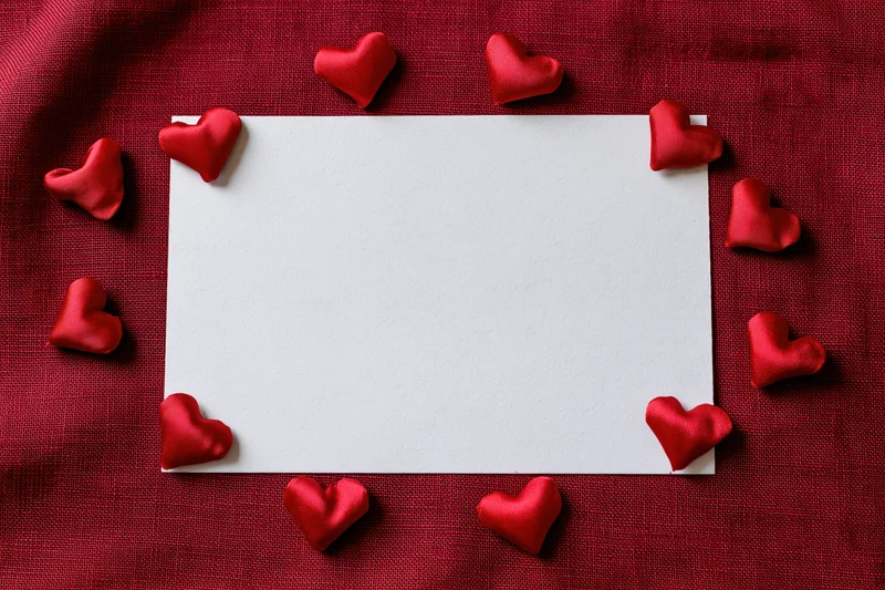 Blank white card surrounded by red hearts on red fabric surface