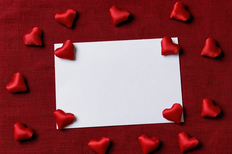 Blank white card centered on red fabric surrounded by red satin hearts