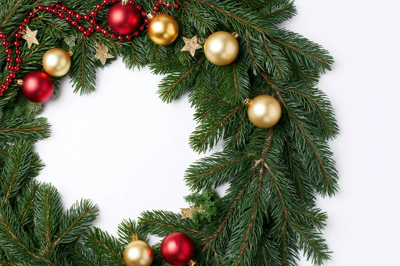 Christmas wreath made of fresh fir branches decorated with red and gold ornaments arranged in a circular frame on white background