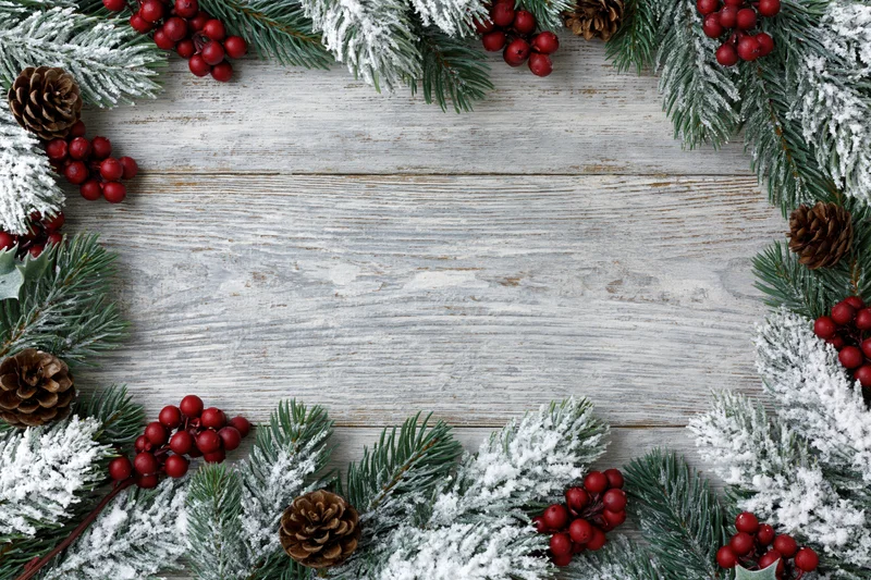 Snow-dusted fir branches and red berries arranged in a border on a rustic wooden surface