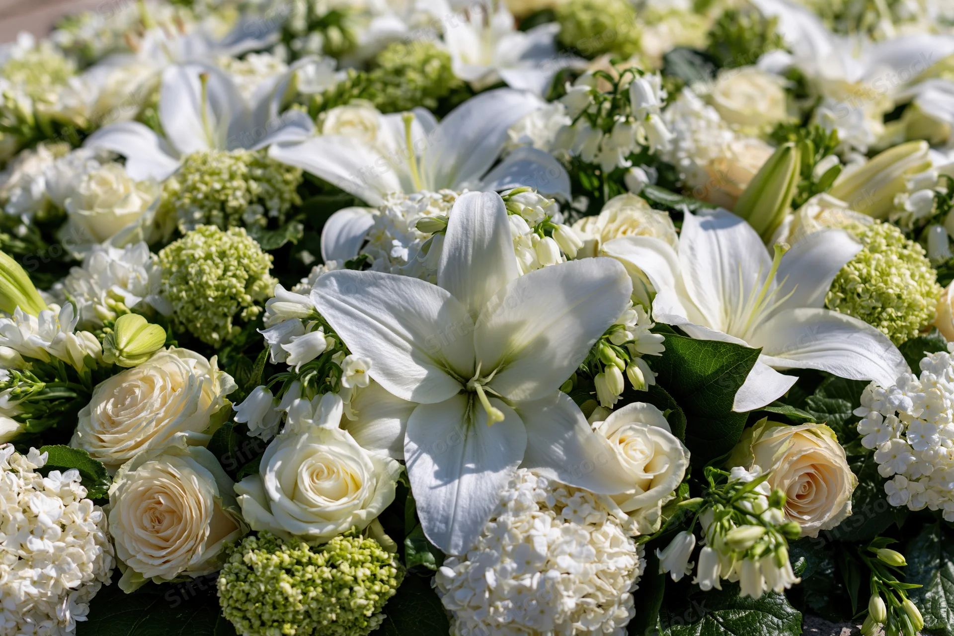 Dense white floral arrangement with lilies and roses laid flat outdoors for funeral tribute