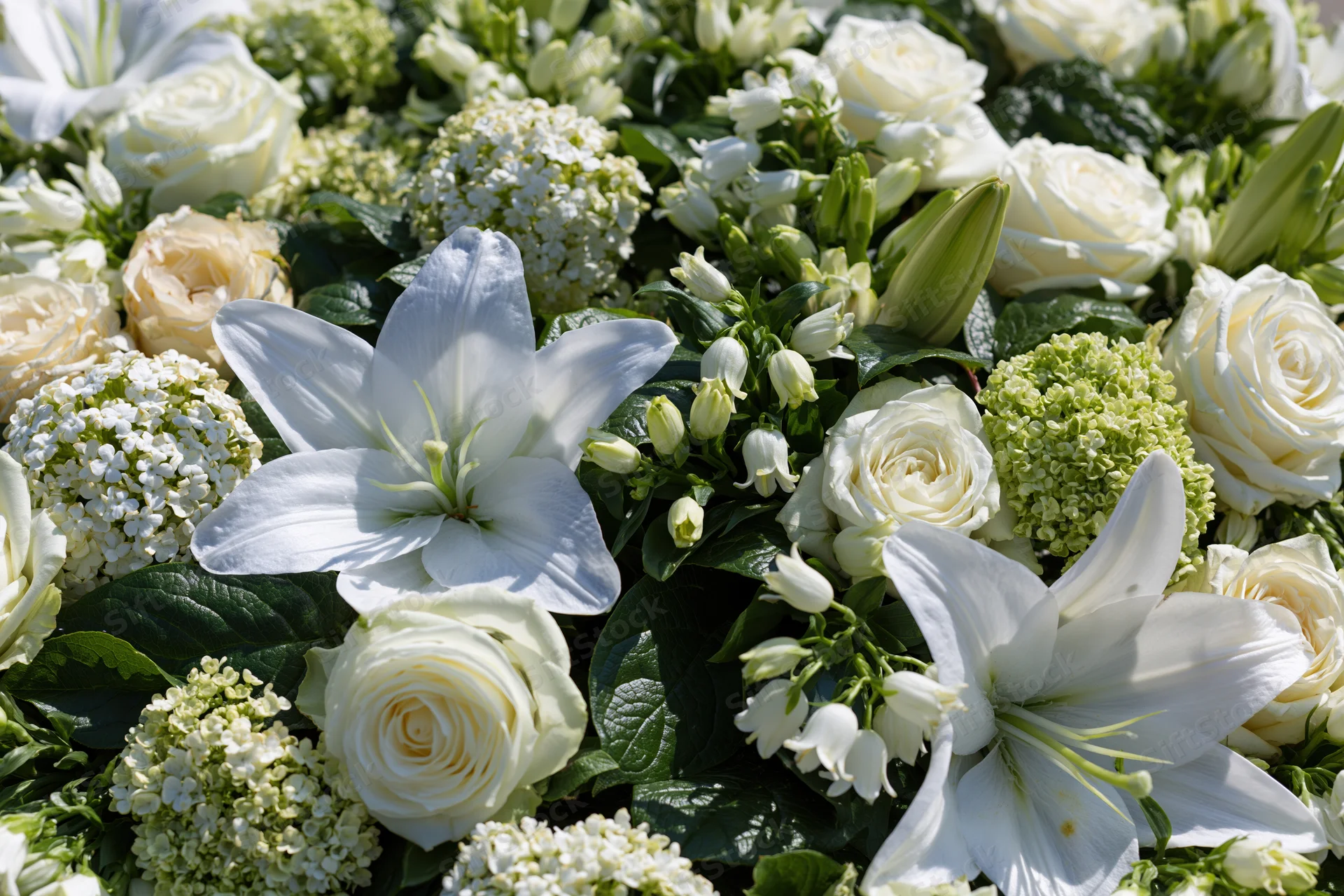 Dense white floral arrangement with lilies, roses, and hydrangeas laid flat outdoors