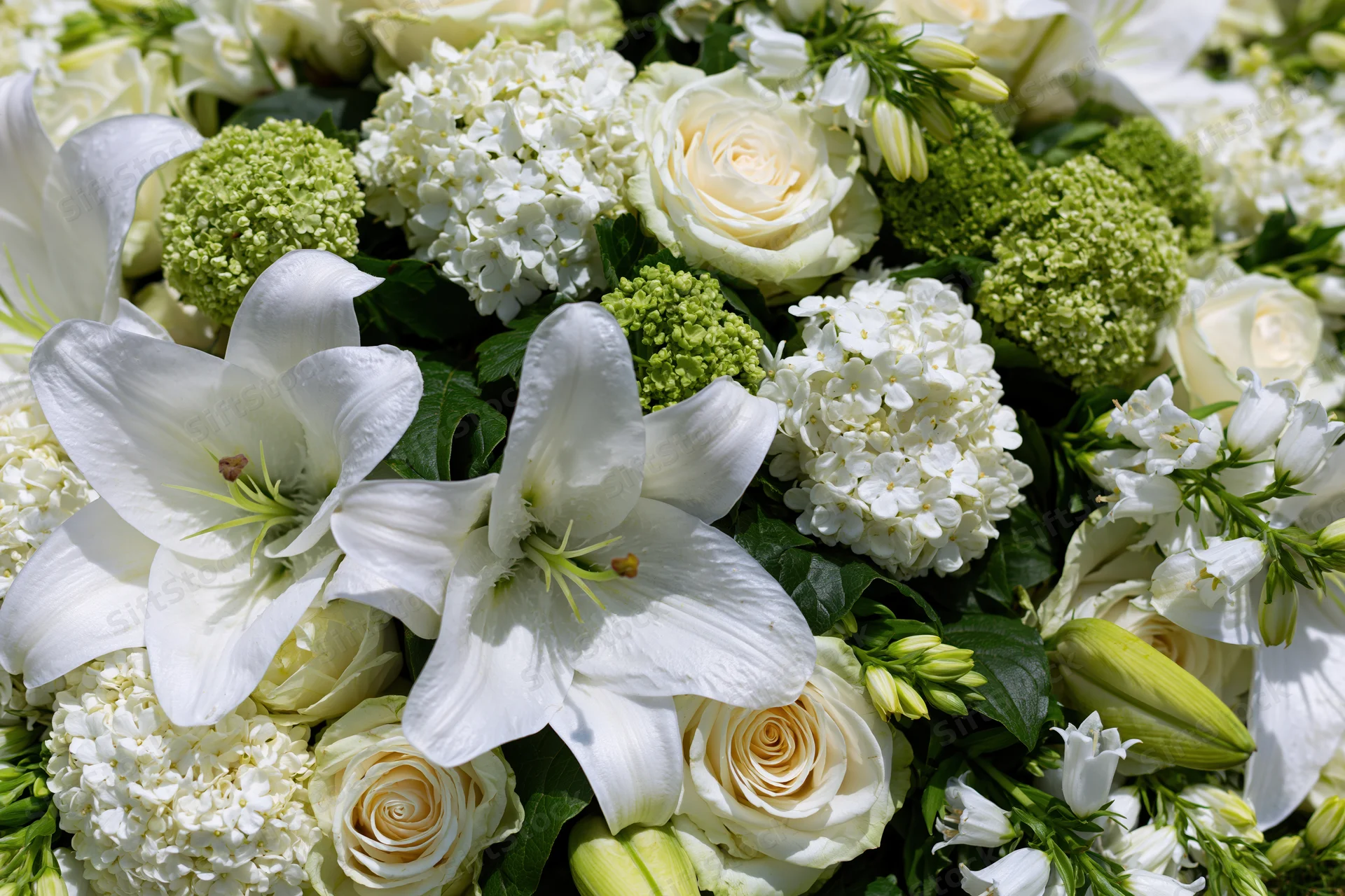 Close-up of a dense white floral arrangement with lilies, roses and hydrangeas laid flat on a surface