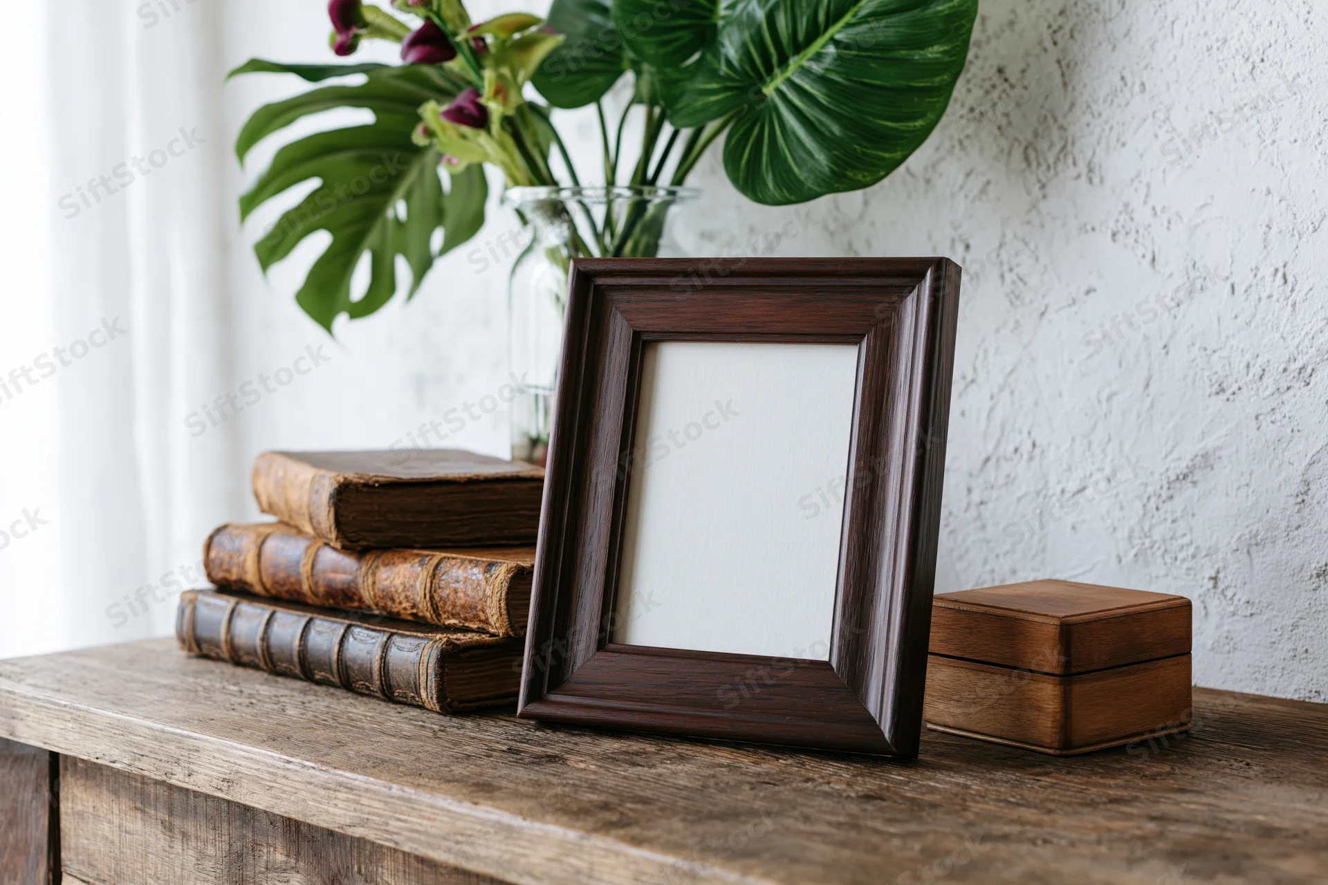 Dark wood picture frame with blank white insert leaning on wooden shelf beside stack of vintage books and potted plant
