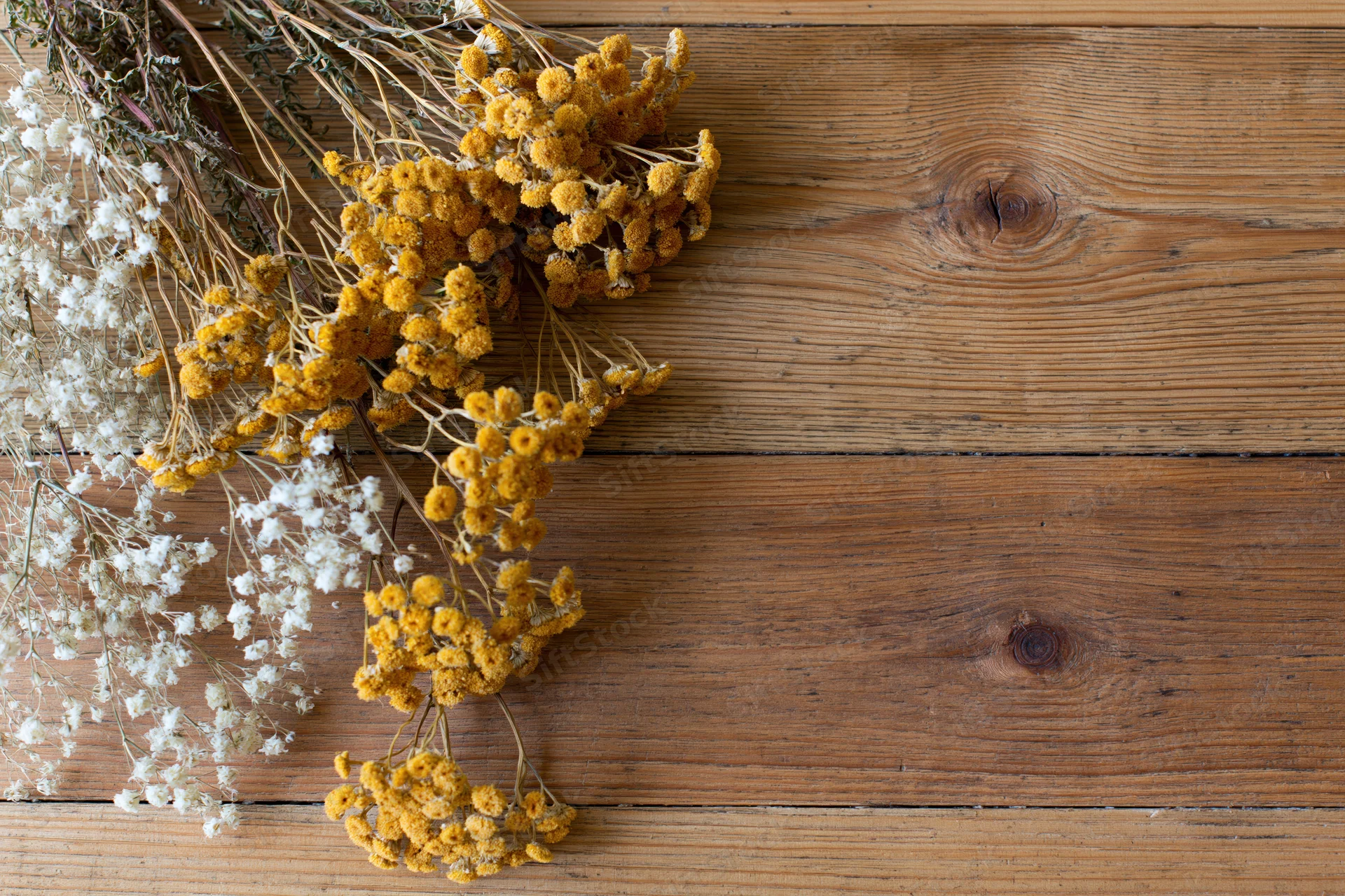 Dried wildflowers and tansy blooms arranged on a rustic wooden table with copyspace