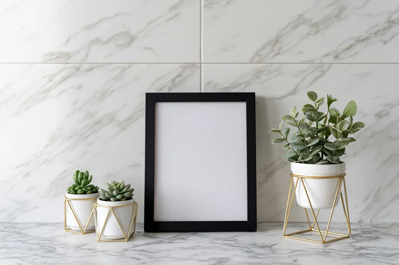 Empty black picture frame leaning against white marble wall with potted succulents on countertop