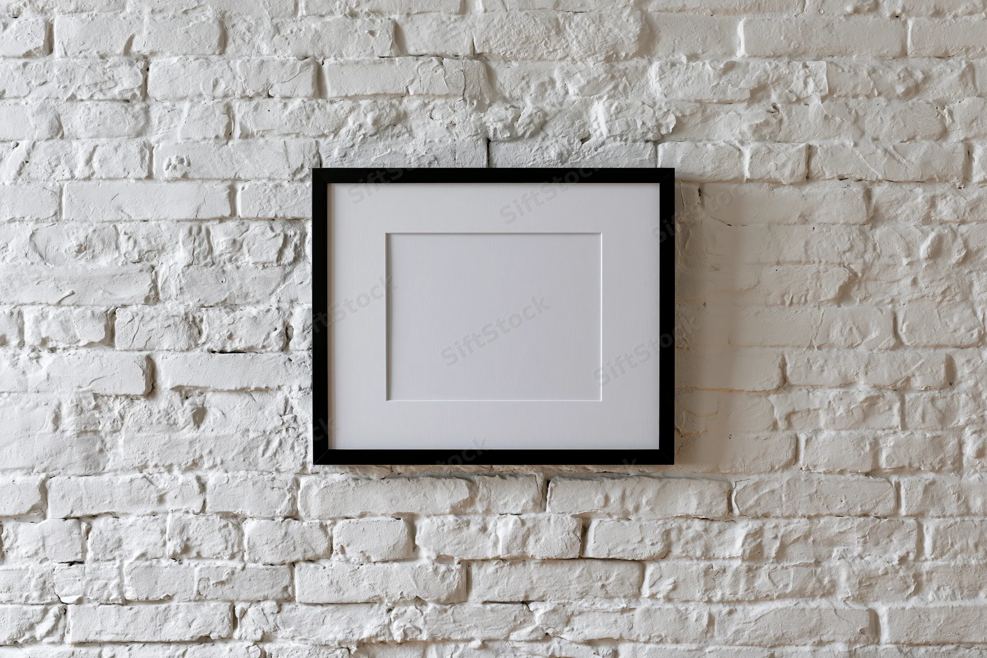 Black picture frame with white mat hanging centered on white brick wall