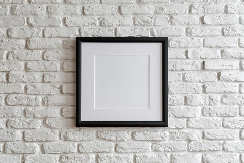 Black picture frame with white mat hanging centered on white brick wall