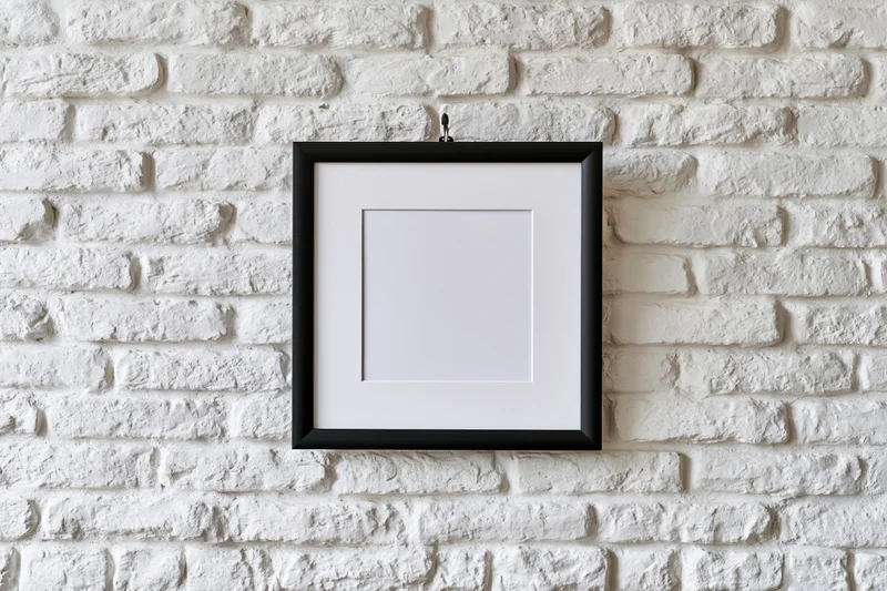 Black picture frame with white mat hanging centered on white brick wall