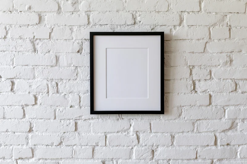 Black picture frame with white mat hanging centered on white brick wall