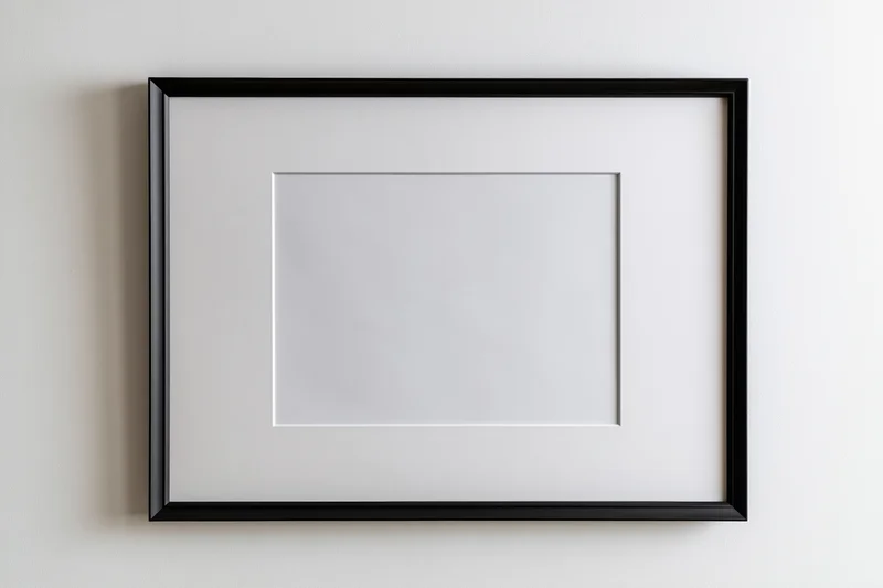 Black picture frame with white mat mounted on white wall, empty interior space for artwork display