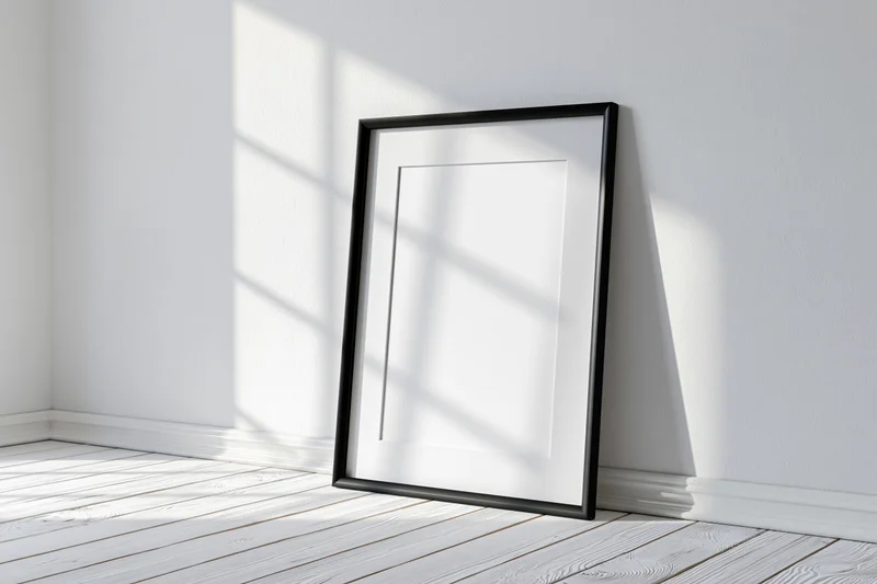 Black picture frame with white mat leaning against white wall in minimalist room