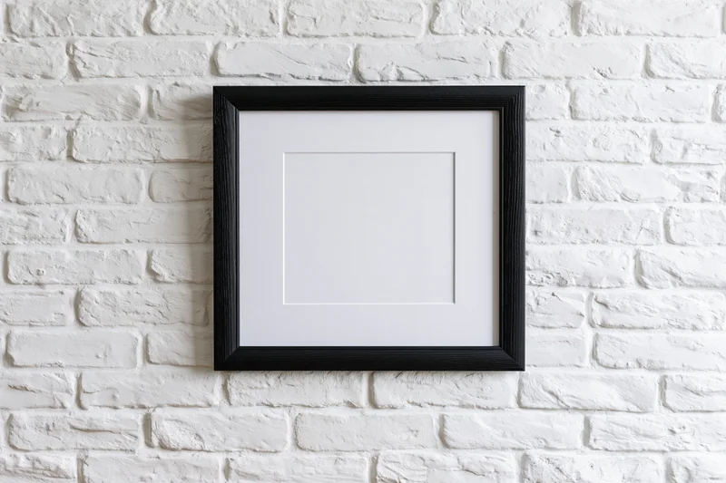 Black wooden picture frame with white mat hanging on white brick wall